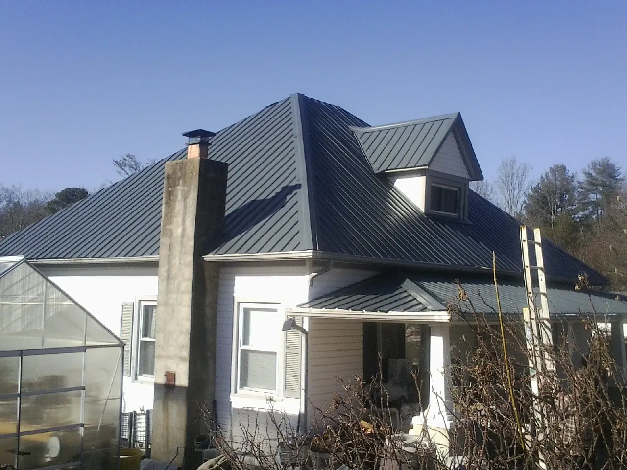 Dark blue standing seam metal roof on a white farmhouse with dormer — Slate & Tile Roof Repair by Roofing Brothers in Saucier