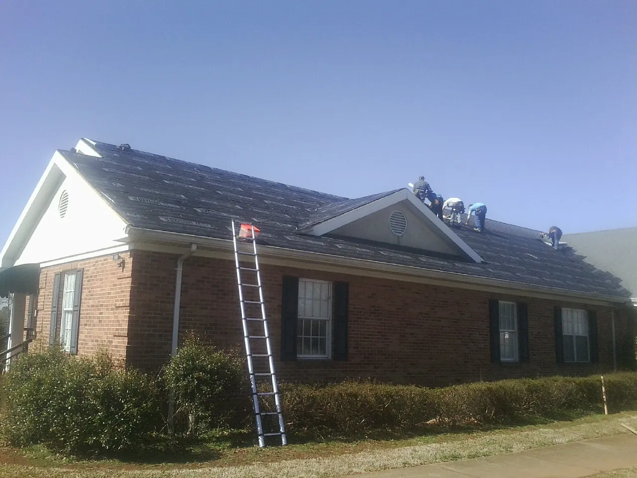 Crew tearing shingles off a brick ranch roof with a ladder set — Emergency Roof Repair work by our crew in Saucier