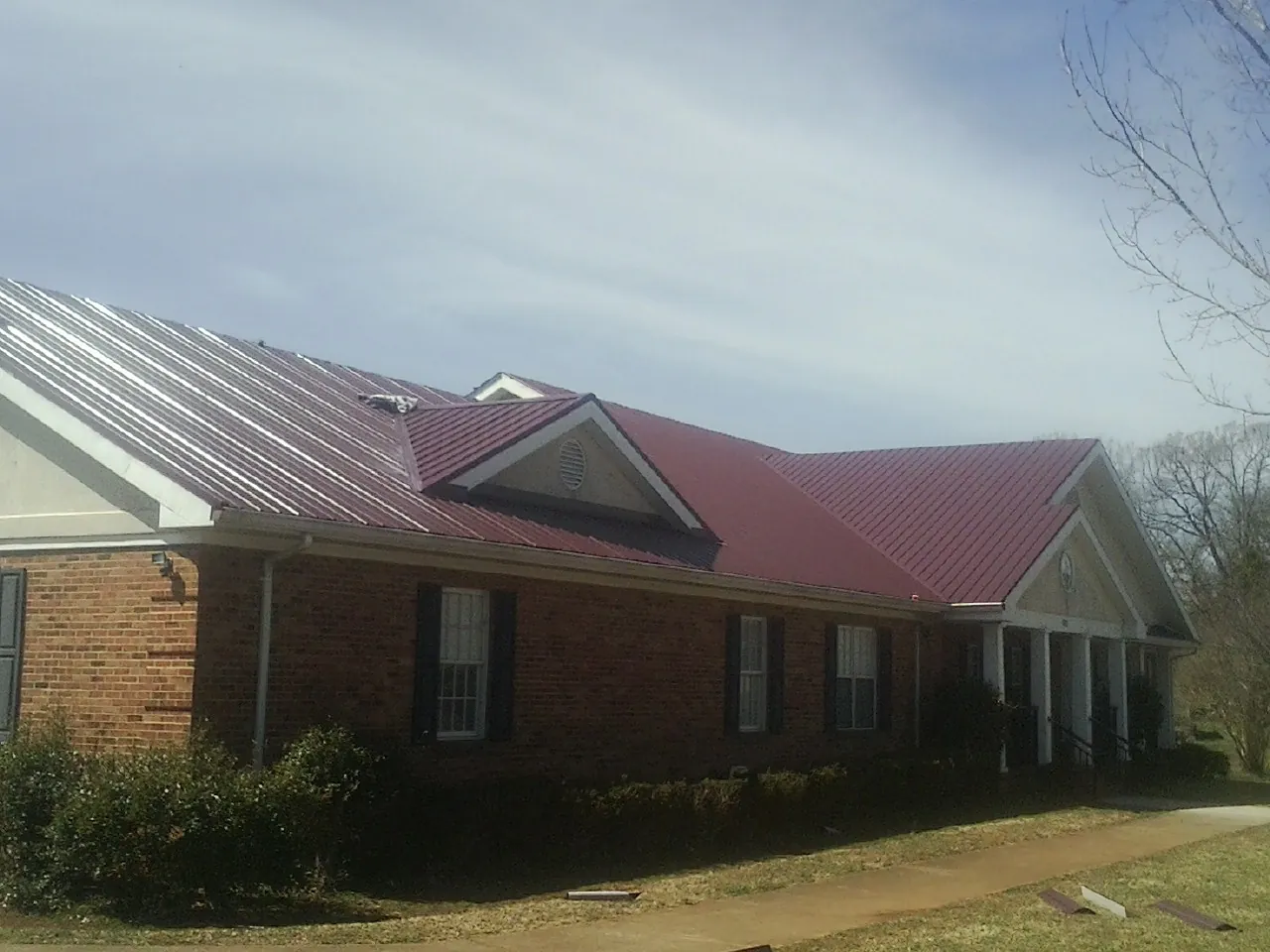 Red metal roof with gabled entries on a long brick building, from a Hail Damage Roof Repair job in Saucier