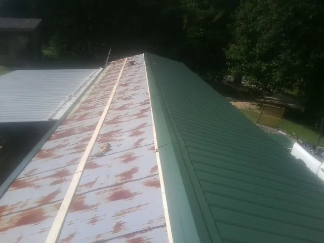 Old rusted panels beside newly installed green metal roofing — Wind Damage Roof Repair by Roofing Brothers in Saucier
